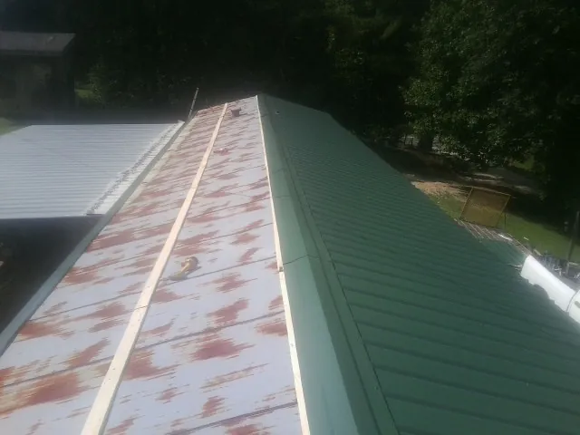 Old rusted panels beside newly installed green metal roofing — Wind Damage Roof Repair by Roofing Brothers in Afton