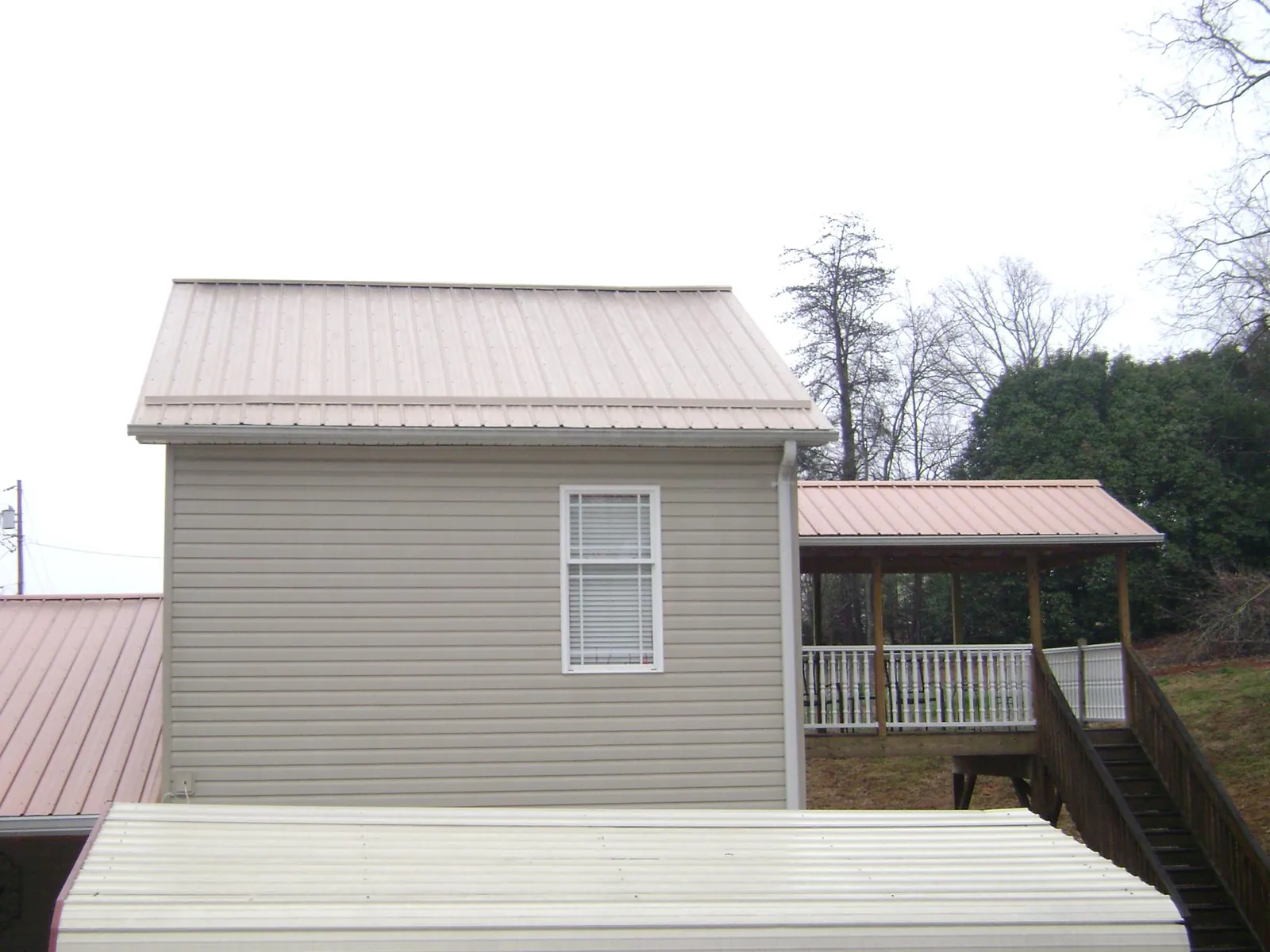 Tan metal roofs on a two story addition and attached porch, from a Roof Replacement job in Afton